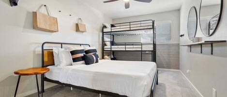 A bedroom with a bunk bed, a single bed, a ceiling fan, and a mirror on the wall.