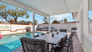 A poolside patio with a table and chairs, a pool, and a view of a white wall with the word "dale" partially visible. - Heated Pool, Fire Pit, Games & Outdoor Dining Just Minutes to Old Town Drift House by Avantstay (Scottsdale)