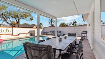 Un patio junto a la piscina con una mesa y sillas, una piscina y vistas a una pared blanca con la palabra "dale" a la vista.