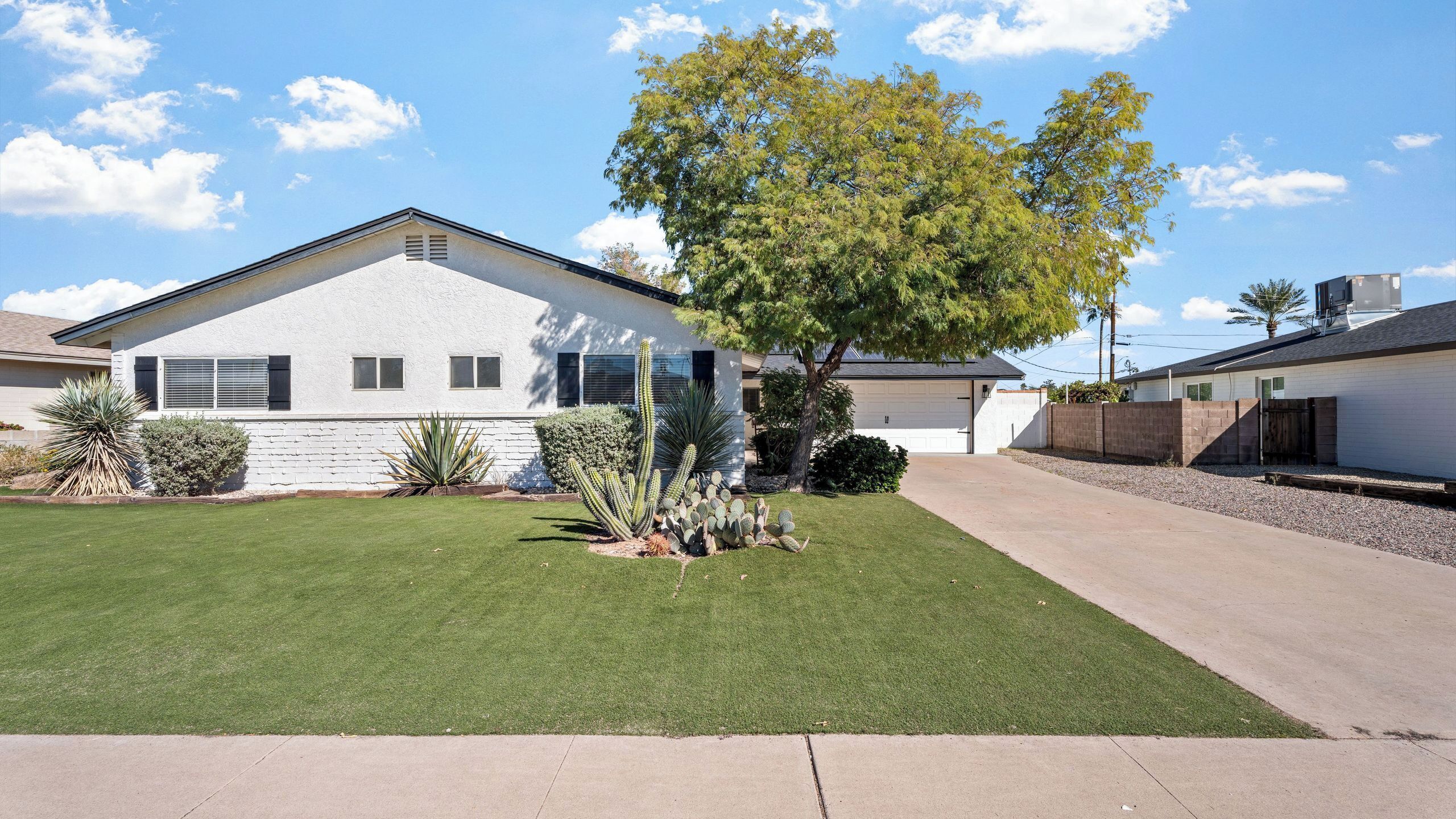 A single-story house with a white exterior, a front yard with green grass, and a tree.