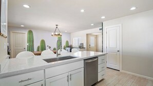 A modern kitchen with white cabinetry, a central island with a sink, and a ceiling light fixture. - Heated Pool, Fire Pit, Games & Outdoor Dining Just Minutes to Old Town Drift House by Avantstay (Scottsdale)