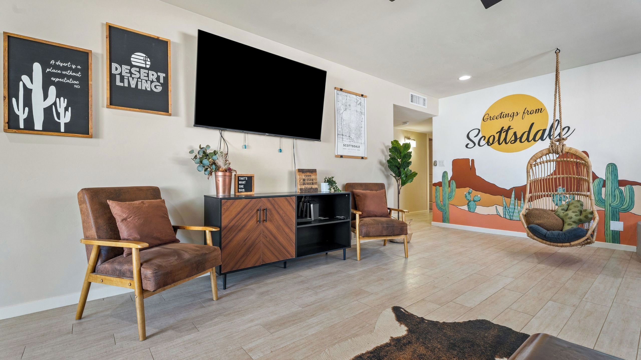 A living room with a flat-screen TV, two brown leather chairs, a wooden cabinet, and a hanging chair.