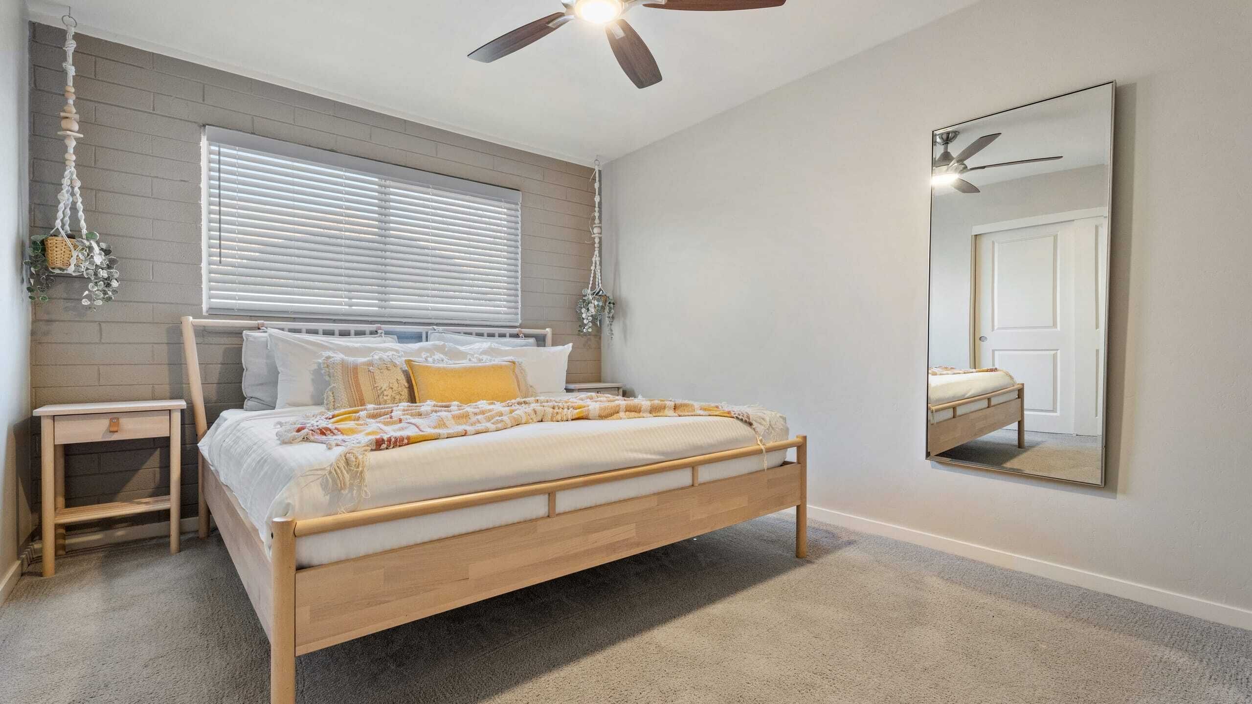 Un dormitorio con una cama de madera, una mesita de noche, un ventilador de techo y un espejo grande.