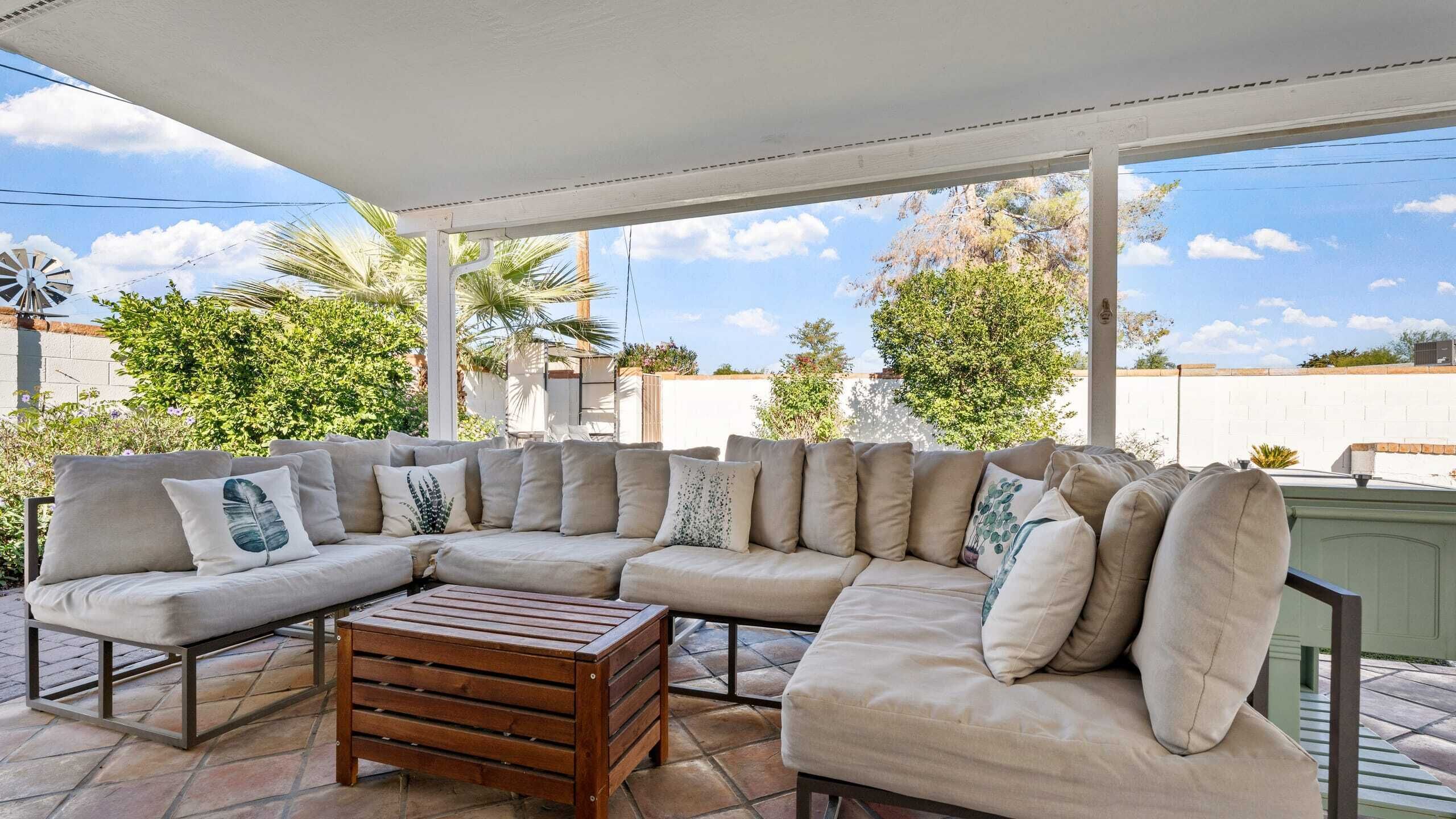 A covered outdoor seating area with a sectional sofa and a wooden coffee table.
