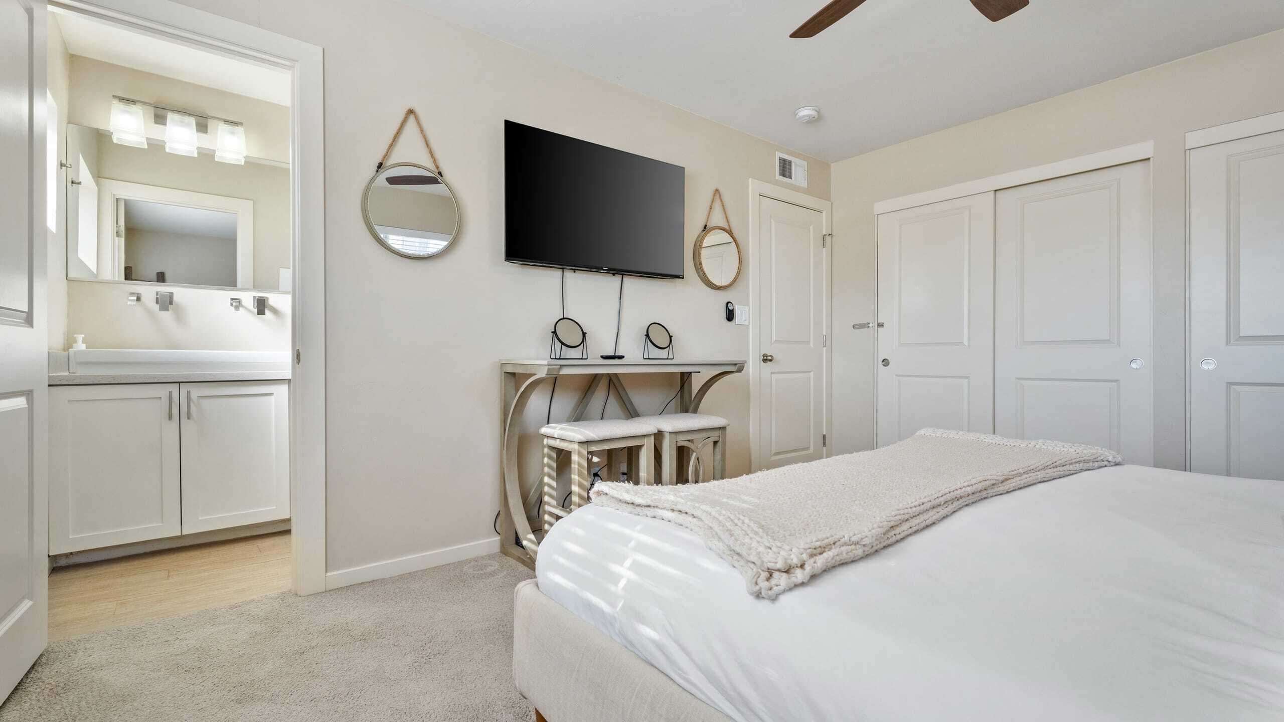 Ein Schlafzimmer mit Bett, Fernseher, Schminktisch und Spiegel sowie einer Tür.
