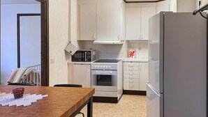 Une cuisine de taille réduite, avec des meubles blancs, un four à micro-ondes, un four traditionnel et un réfrigérateur.