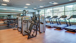 Une salle de sport équipée de machines de cardio, d’appareils de musculation et d’un grand miroir.