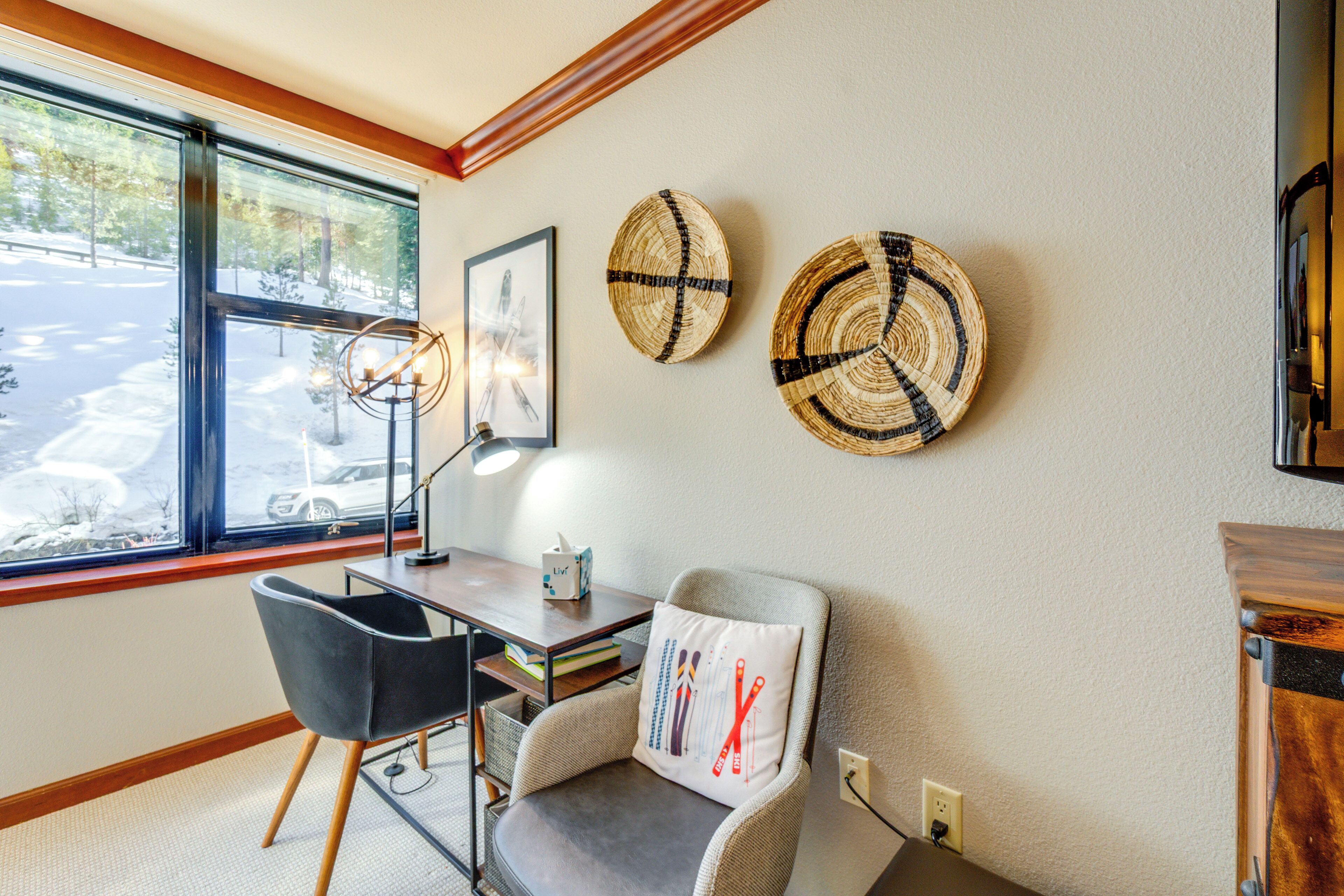 A room with a desk, chair, and two woven wall decorations.