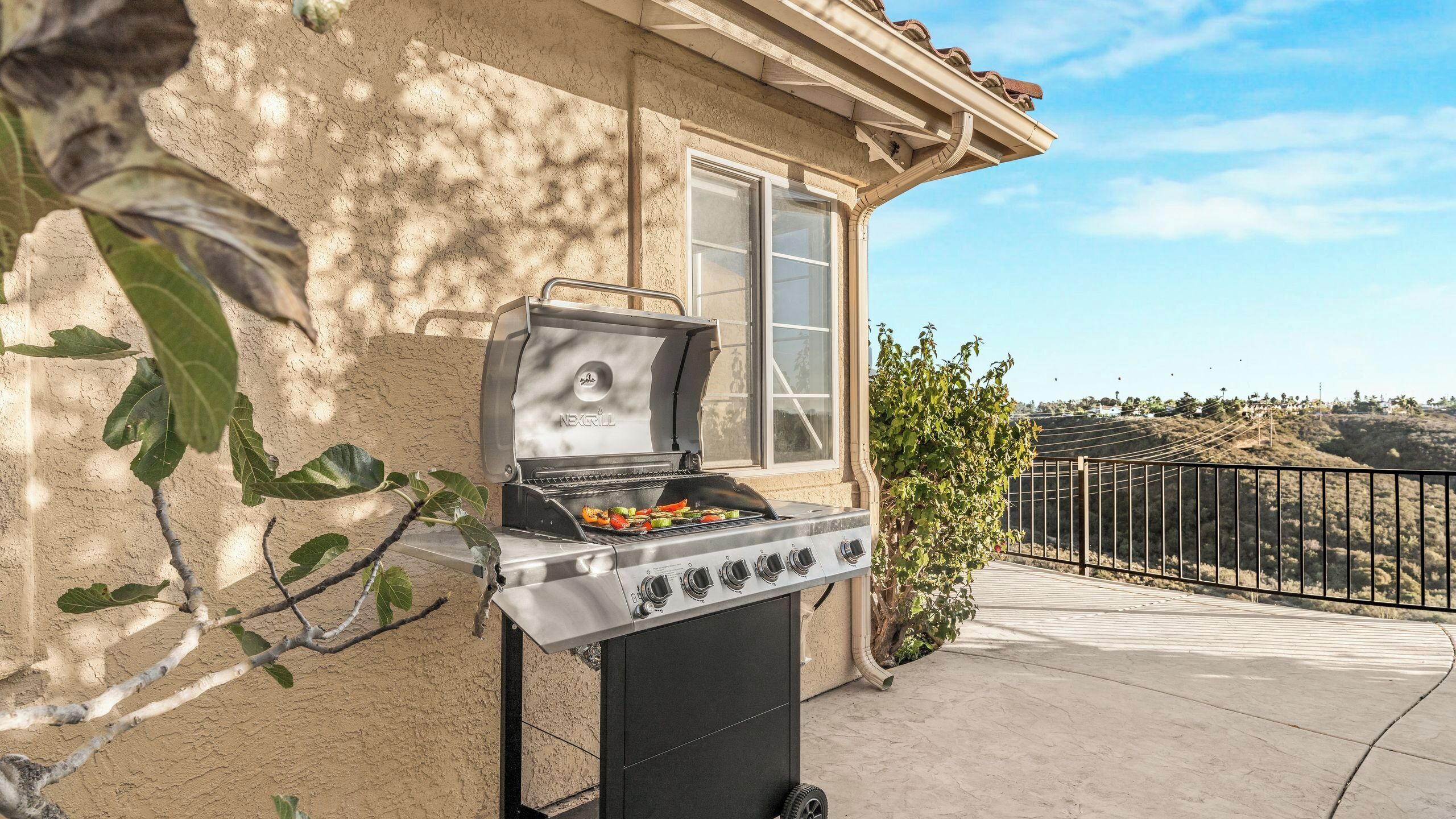 A portable grill with vegetables on it, positioned on a balcony with a view of a hilly landscape.