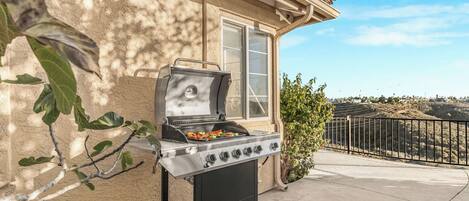 A portable grill with vegetables on it, positioned on a balcony with a view of a hilly landscape.