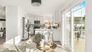 A modern kitchen with white cabinetry, stainless steel appliances, and a dining area with a round table and chairs. - Vista del Sol by Avantstay Bright Hilltop Stay + Patio + Views + Premium Kitchen & Space for Groups (San Diego)
