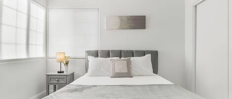 Une chambre à coucher avec un lit, une table de chevet, une lampe et une œuvre d’art accrochée au mur.