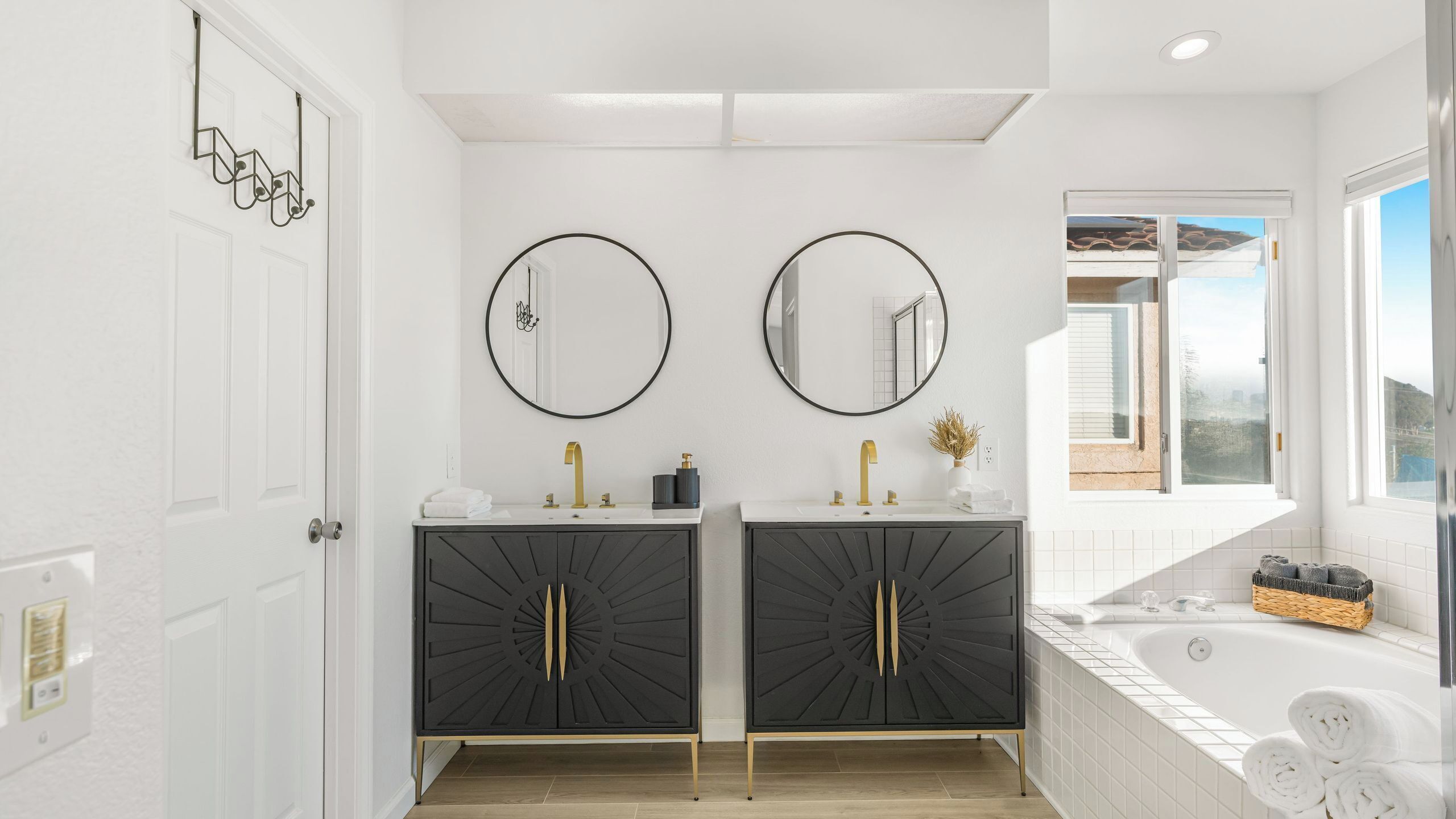 A bathroom with two sinks, black cabinets, gold fixtures, and a bathtub.