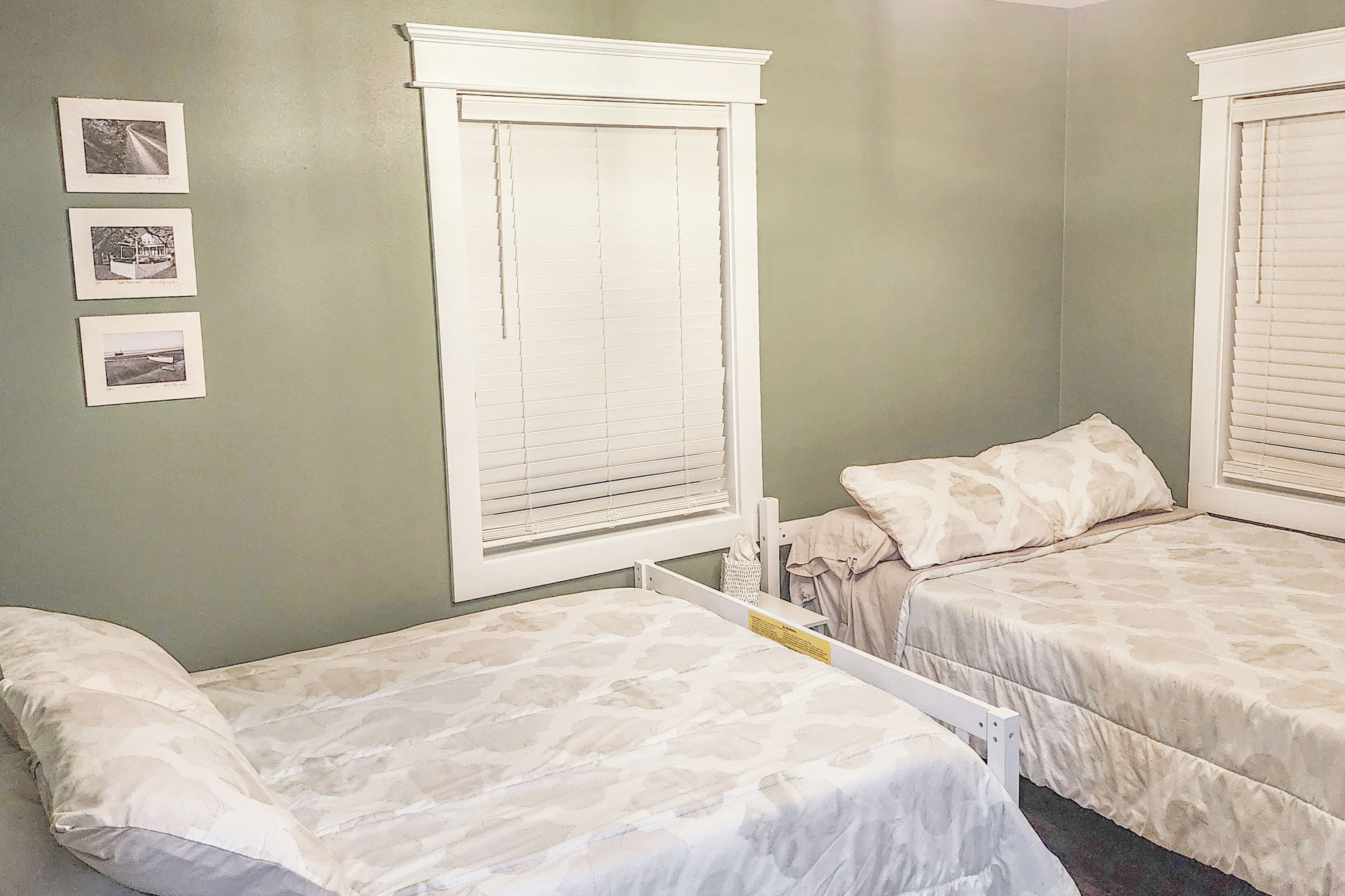 Une chambre avec deux lits, une fenêtre avec des stores et trois tableaux encadrés accrochés au mur.