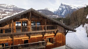 Eine Holzhütte mit Balkon vor einer verschneiten Berglandschaft.