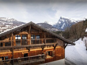 Un chalet en bois doté d’un balcon, situé au pied d’une montagne enneigée.