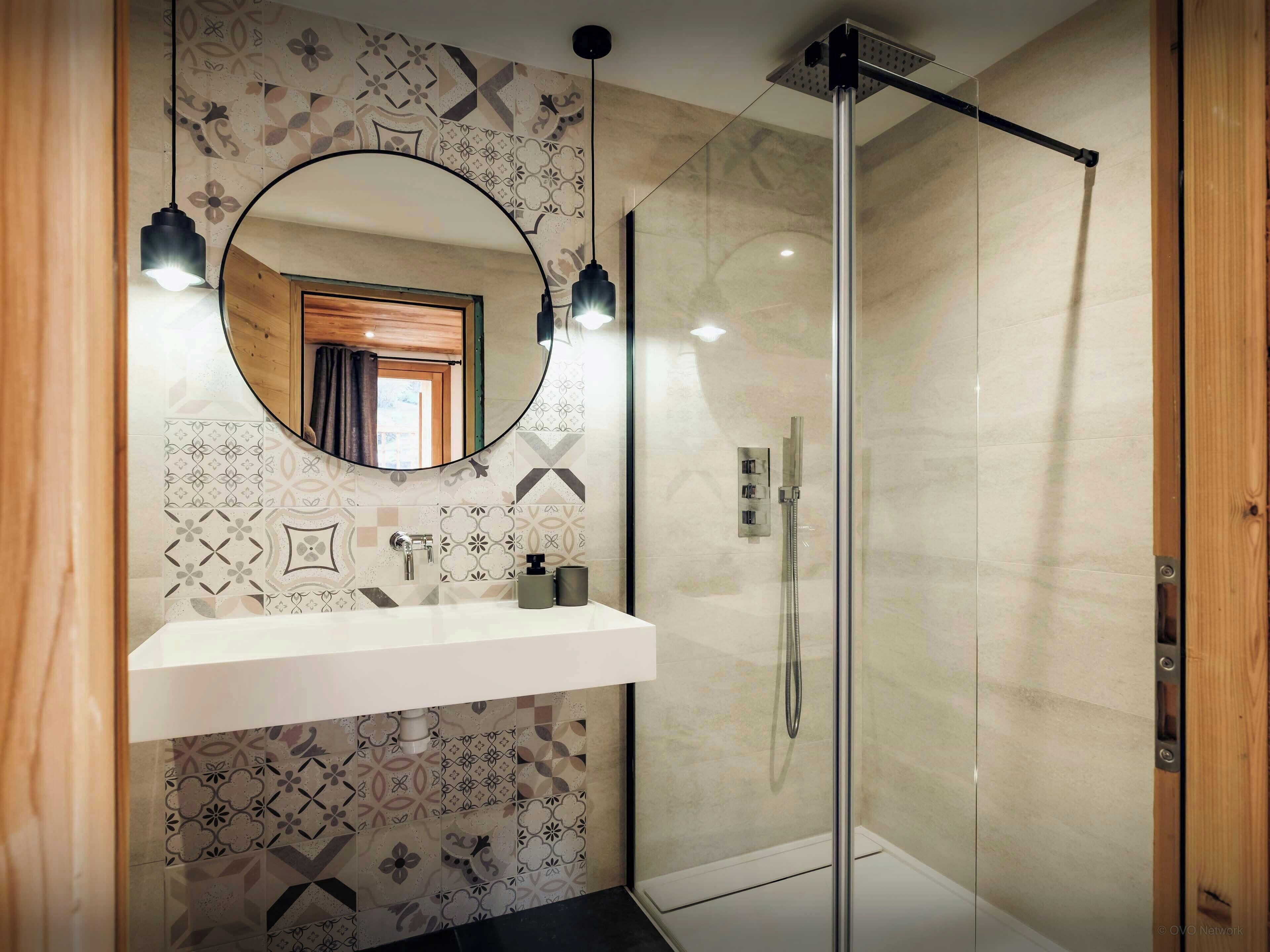 A bathroom with a glass shower enclosure, a wooden-framed mirror, and a patterned tile backsplash.