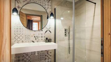 A bathroom with a glass shower enclosure, a wooden-framed mirror, and a patterned tile backsplash.