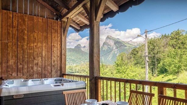 Eine Holzhütte mit Whirlpool, Esstisch mit Brot und Tassen sowie Blick auf die Berge.