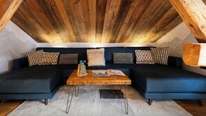 Ein gemütliches Lofts-Zimmer mit einer dunkelblauen Sofagarnitur, einem Holztisch und einem weißen Shaggy-Teppich.