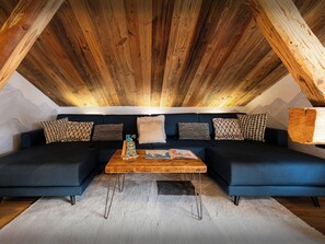 A cozy loft-style room with a dark blue sofa set, a wooden coffee table, and a white shag rug.