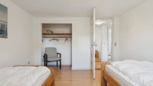 A room with two beds, a chair, a shelf with hanging items, and a door leading to another room.