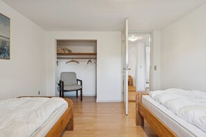A room with two beds, a chair, a shelf with hanging items, and a door leading to another room. - Calm holiday home with great outings (Kruså)