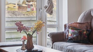 A room with a window, a table with a vase of flowers, and a sofa with a colorful pillow.