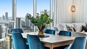 Uma sala de jantar moderna com vista para a cidade, uma mesa com cadeiras azuis e um vaso com plantas verdes.