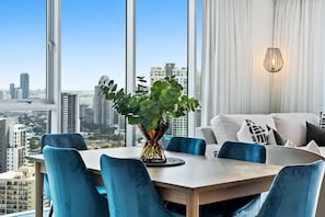 Ein moderner Essbereich mit Blick auf die Stadt, ein Tisch mit blauen Stühlen und eine Vase mit Grünpflanzen.