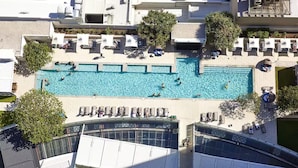 Vista aérea de um hotel com várias piscinas, espreguiçadeiras e uma área coberta com guarda-sóis.