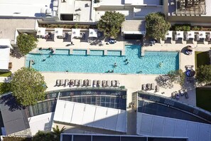 Eine Vogelperspektive auf ein Hotel mit mehreren Swimmingpools, Liegestühlen und einem überdachten Bereich mit Sonnenschirmen.