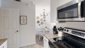 Una cuina moderna amb armaris blancs, microones d'acer inoxidable, fogó negre i zona de menjador amb taula i caires blancs.