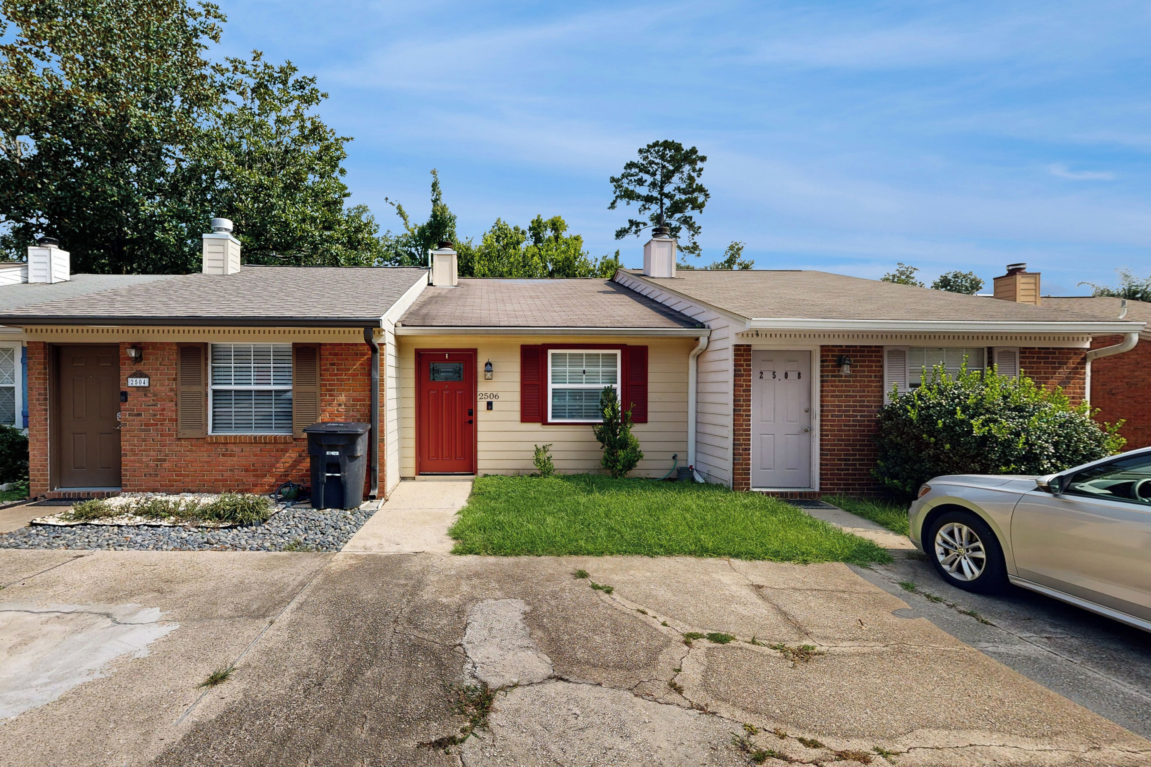A two-story residential house with a brick facade, a red front door, and a beige exterior.