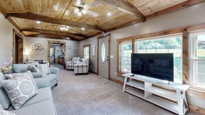 Un salon spacieux avec une grande télévision, des poutres apparentes en bois au plafond et un coin salon confortable.