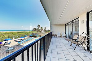 Un balcon avec vue sur la plage, des chaises longues et des parasols.
