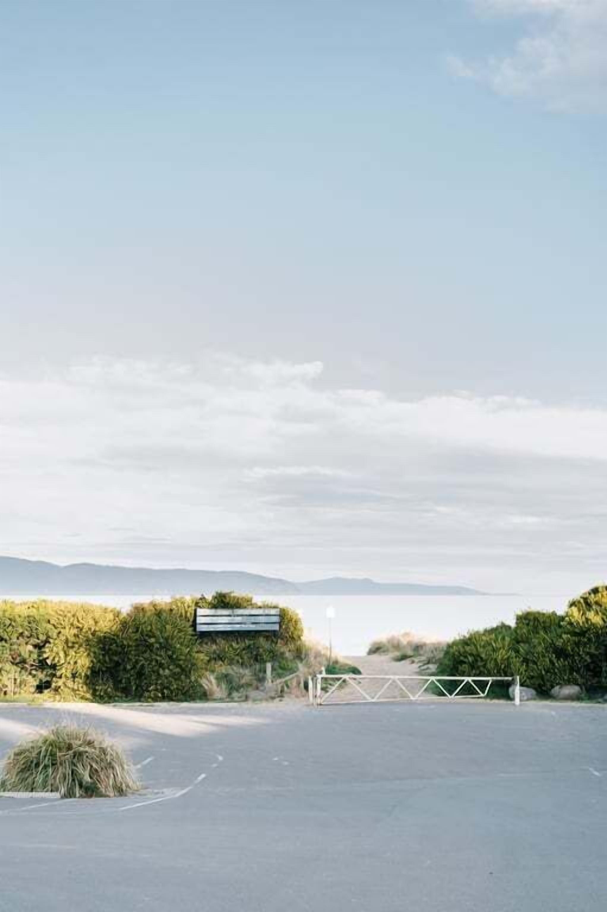 A parking lot with a gated entrance, a signboard, and a view of distant hills.