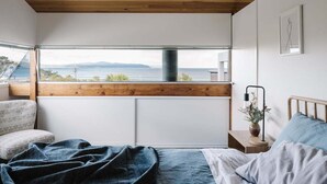 Un dormitorio con un ventanal grande que da a una masa de agua y tierra distante.