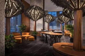 A modern lobby with a central dining area, seating arrangements, and decorative lighting fixtures. - Luxury Downtown San Diego Condo; High-Floor Epic Views + Resort-Style Amenities (San Diego)