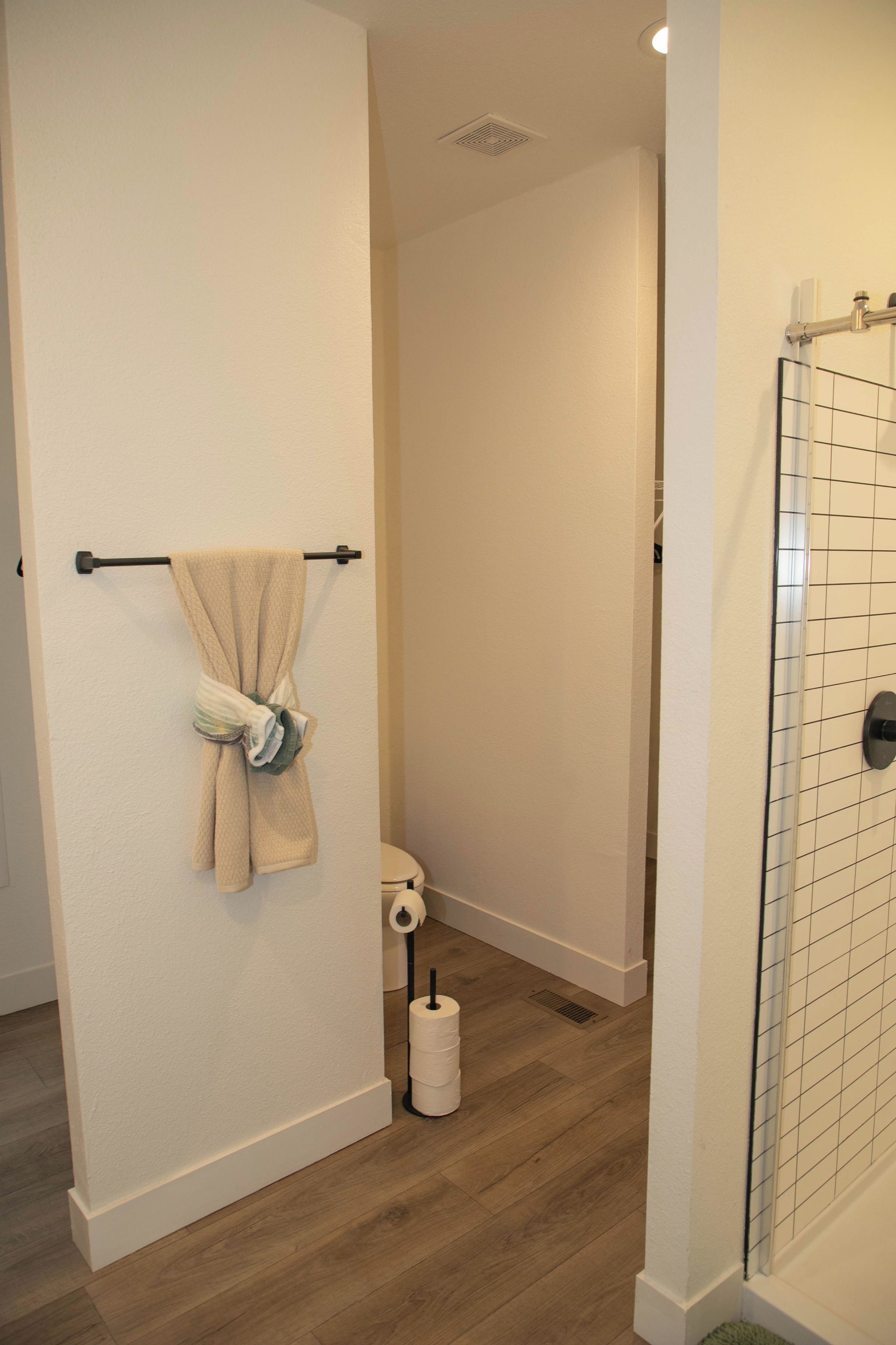 Une salle de bain comprenant des toilettes, un porte-serviettes avec une serviette, un support à papier toilette et un espace douche doté d’une porte en verre.