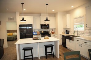 A modern kitchen with white cabinets, stainless steel appliances, a central island with stools, and pendant lighting. - Enjoyable 4-bedroom house with AC in charming Taylor.  (Taylor)