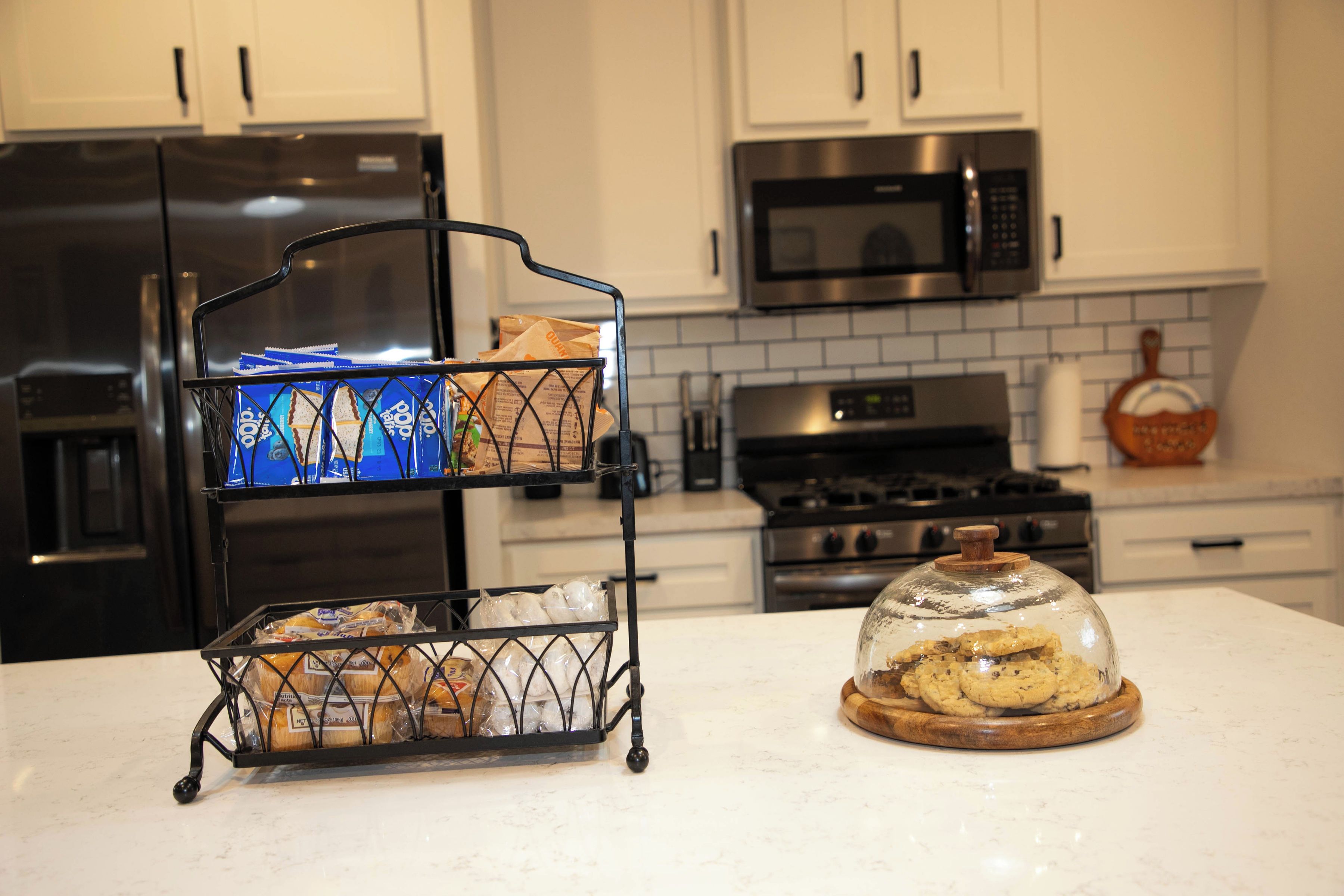 A kitchen with a bread rack holding packaged bread and a glass dome displaying cookies.
