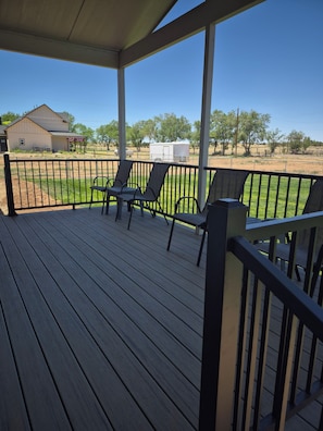 Una terraza techada al aire libre con suelo de madera y barandillas de metal, con dos sillas y una mesa.