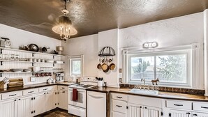 Una cocina con armarios blancos, piso de madera y ventana con vista a árboles.