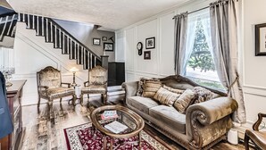 Una sala de estar con una escalera, un sofá, dos sillones, una mesa de centro y una alfombra.