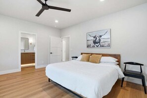 A bedroom with a bed, a ceiling fan, a door, and a wall-mounted picture of a cow.