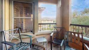 A balcony with a view of neighboring buildings, a chair, a small table, and a window with blinds. - Balcony & Pool Access! Extended Stay in Scottsdale (Scottsdale)