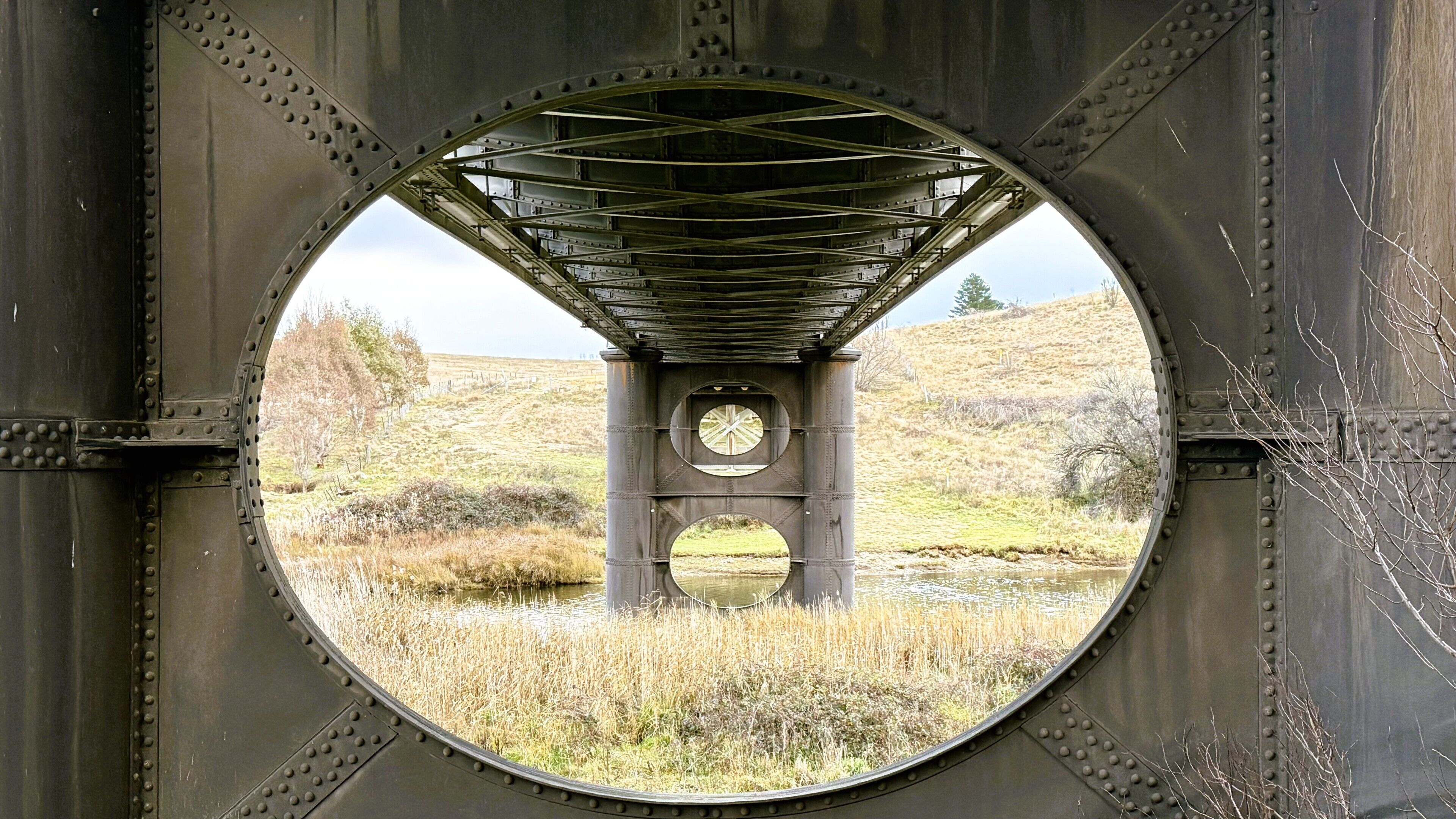 A circular window with a clock and a view of a grassy landscape.