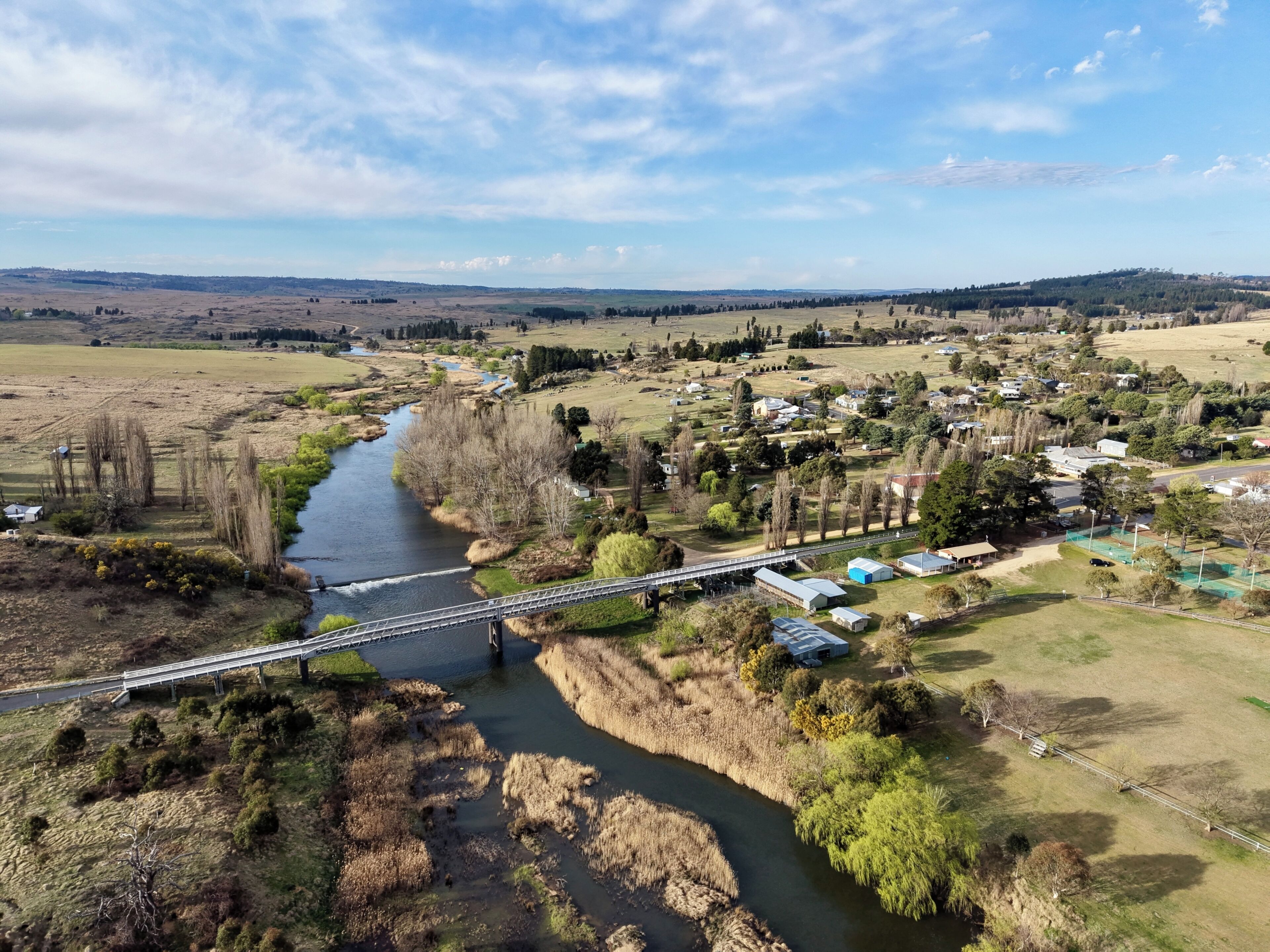 A river flowing through a rural landscape with a bridge, houses, and greenery.
