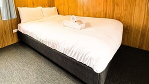 A neatly made bed with white linens, a dark headboard, and a framed picture on the wall. - Snowy River Holiday Park (Dalgety)